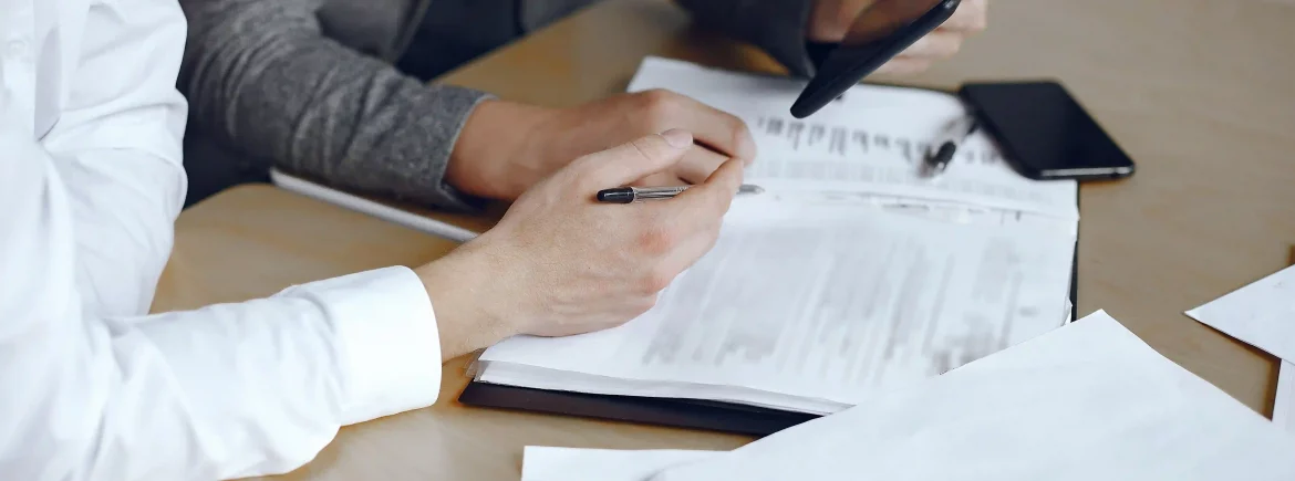 Primer plano de profesionales revisando contratos y documentación técnica de obra sobre una mesa, representando la gestión administrativa de Renova para evitar el estrés burocrático.