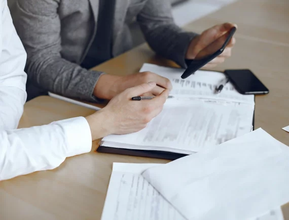 Primer plano de profesionales revisando contratos y documentación técnica de obra sobre una mesa, representando la gestión administrativa de Renova para evitar el estrés burocrático.